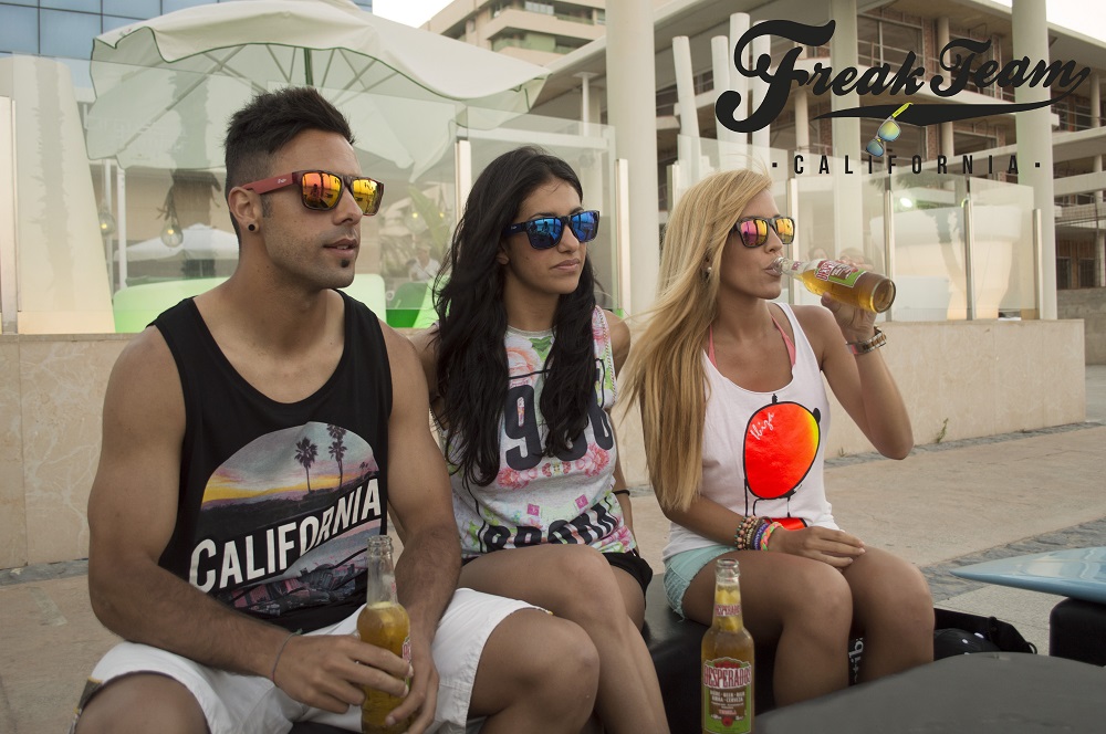 foto con el logo antiguo de freak team de 3 chicos sentados en el paseo marítimo vistiendo gafas de sol